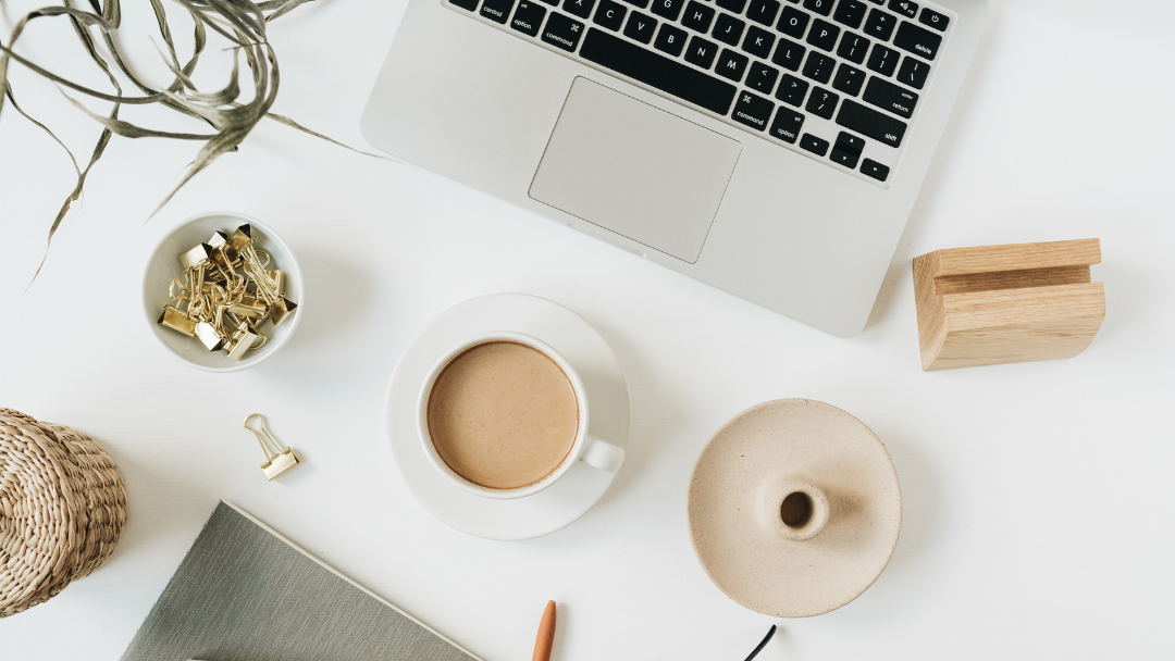 Laptop on a white desk with a cup of coffee, notebook, and decorative items.